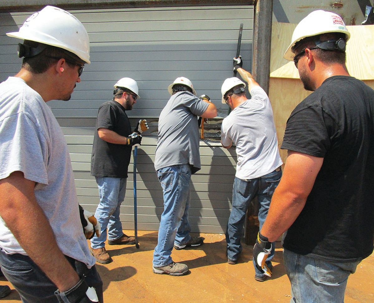 Three men attempt breaking down a door with crowbars while two other men watch