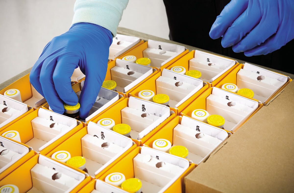 Packing custom kits - A disembodied hand places a reagent vial into a kit box within an open flat of kits during assembly