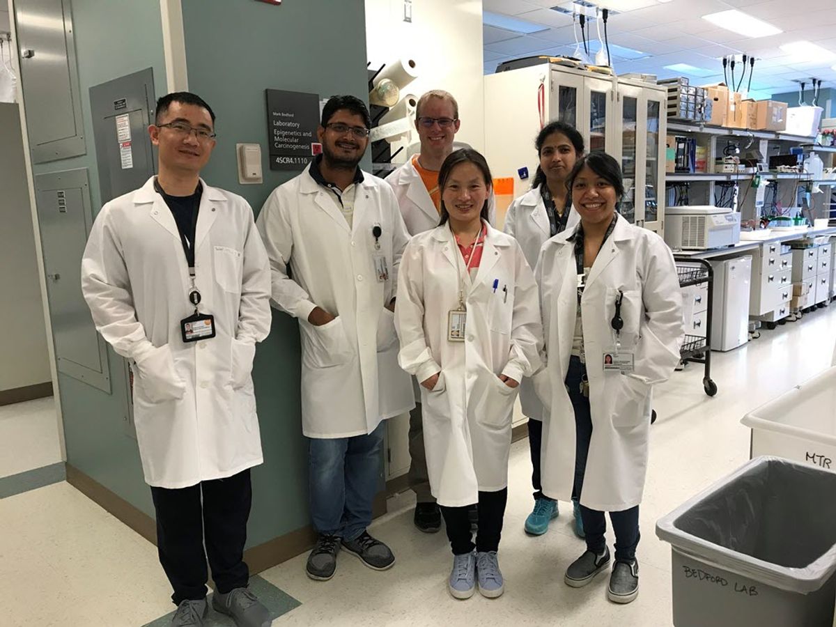 group photo of staff from the Bedford Lab at MD Anderson Cancer Center posing in a lab aisle